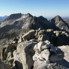 Cumbre rocosa con cairn, vista panorámica de montañas escarpadas bajo cielo azul. Besiberri Nord.