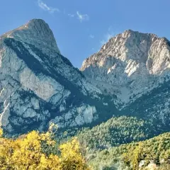 Majestuosas montañas de el Pedraforca bajo un cielo azul. El sol ilumina las cumbres rocosas y los bosques verdes.