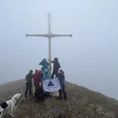 Grupo de montañistas celebra en la cima con un perro, bajo un gran taga y neblina.