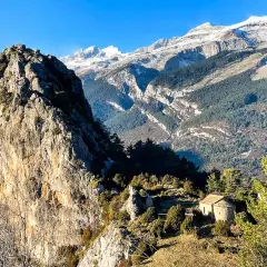Pequeña ermita de Tella en un paisaje montañoso con picos nevados al fondo.