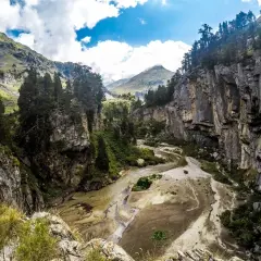 El forau de Aigualluts desde los Llanos del Hospital, un cañón rocoso con un río seco y vegetación verde bajo un cielo azul con nubes.