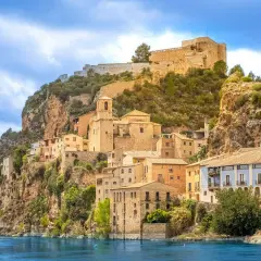Pueblo de cambrils de muntanya aferrat a un penya-segat rocós, amb cases de colors i un castell imponent al cim.