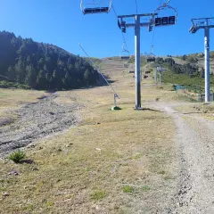 Remontes mecánicos en una ladera verde y rocosa, con la torreta de l orri como punto de referencia.