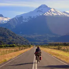 Ciclista pedaleando por la Carretera Austral, con imponentes montañas nevadas de fondo.