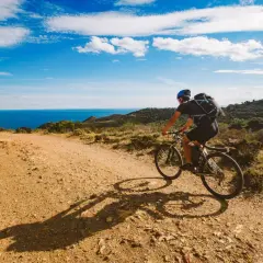 Ciclista disfruta de rutas en bici con encanto por la costa mediterránea. El mar azul y el cielo despejado acompañan su aventura.