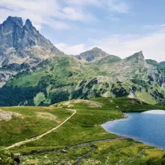 Majestuoso pico en el valle de Ossau, con un lago azul y senderos serpenteantes entre verdes colinas.