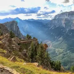 Sendero de piedra serpentea por la ladera con vistas a un profundo valle en los Pirineos de Huesca.