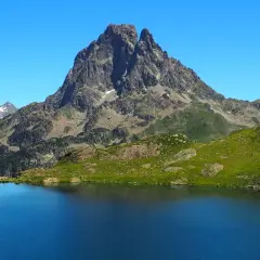 Lago azul intenso reflejando picos rocosos y verdes laderas en los Pirineos Francia.