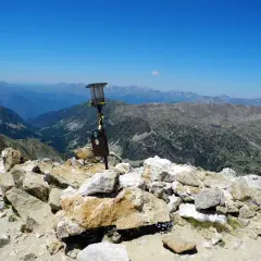 Vistas desde la tossa plana de lles, con un poste de señalización y un paisaje montañoso espectacular bajo un cielo azul.