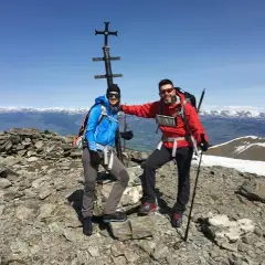 Dos montañistas celebran en la cima del Fontalba Puigmal, con un cruce metálico y vistas nevadas.