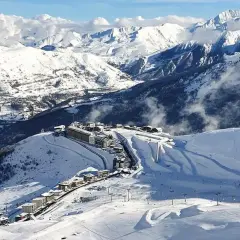 Vista aérea de Saint Lary Soulan, un pueblo de montaña cubierto de nieve con edificios y pistas de esquí, rodeado de majestuosas montañas nevadas.
