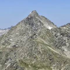 Majestuoso pic de peguera rocoso y escarpado, con nieve en sus cumbres y un cielo azul despejado.
