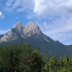 Majestuoso Pedraforca se alza imponente, su altitud desafía las nubes. Bosques verdes cubren sus faldas bajo un cielo azul.