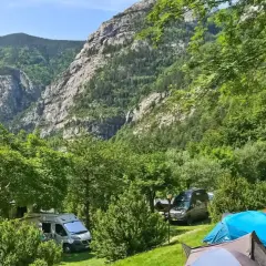 Acampar en este valle es una experiencia de los mejores camping. Tiendas de campaña y furgonetas aparcadas en un prado verde, con imponentes montañas boscosas de fondo.