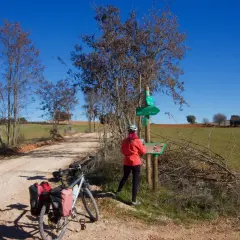 Ciclista consulta señalización en la **vía verde del Tajuña**. Bicicleta con alforjas lista para la aventura.