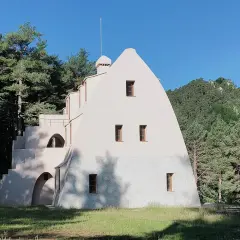 Edificio singular en la Serra de Catllaras, rodeado de pinos y con un cielo azul intenso.