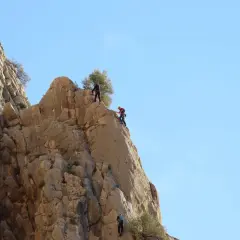 Tres escaladores desafían el chorro escalada en una pared rocosa bajo un cielo azul.