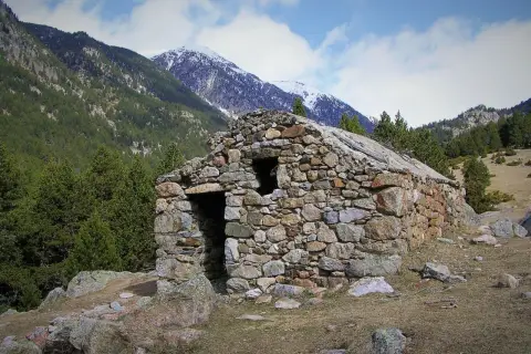 Antigua cabaña de piedra en el Vall de la Llosa, rodeada de pinos y montañas nevadas.