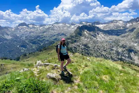 Senderista disfruta de las impresionantes vistas de las rutas del Valle de Arán, con picos nevados y un cielo azul con nubes.