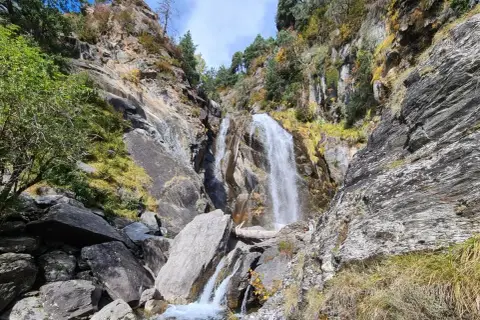 Cascada imponente en la ruta Rupit, rodeada de rocas y vegetación otoñal. El agua cae con fuerza sobre las piedras, creando un paisaje natural espectacular.