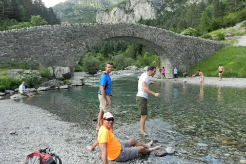 Gente disfrutando del río bajo el puente de piedra en Bujaruelo, con vistas al Taillón.