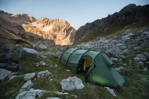 Tienda de campaña verde en un paisaje montañoso rocoso, ideal para acampada libre España.