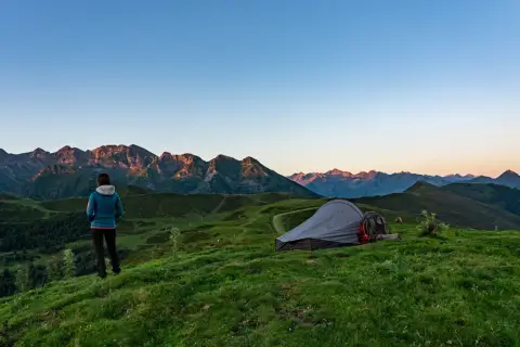 Mujer contempla el amanecer en su acampada libre Francia. Montañas y tienda de campaña en un paisaje idílico.