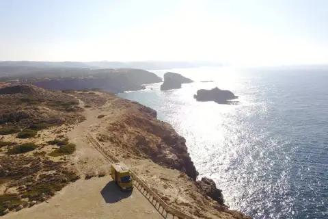Furgoneta amarilla en un acantilado con vistas al mar, ideal para camping en Algarve, Portugal.