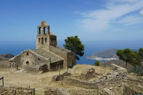 Ruinas de Sant Pere de Rodes, un antiguo monasterio de piedra con vistas al mar Mediterráneo y un pueblo costero.