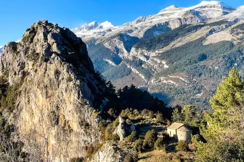 Pequeña ermita de Tella en un paisaje montañoso con picos nevados al fondo.