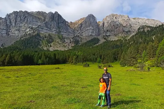 Padre e hijo disfrutan de la ruta Prat del Cadi, con imponentes montañas y un prado verde.