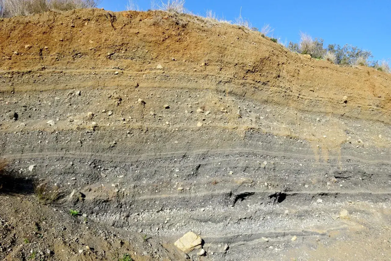Capas de tierra y grava expuestas en un corte, mostrando la geología del volca de la Crosa.