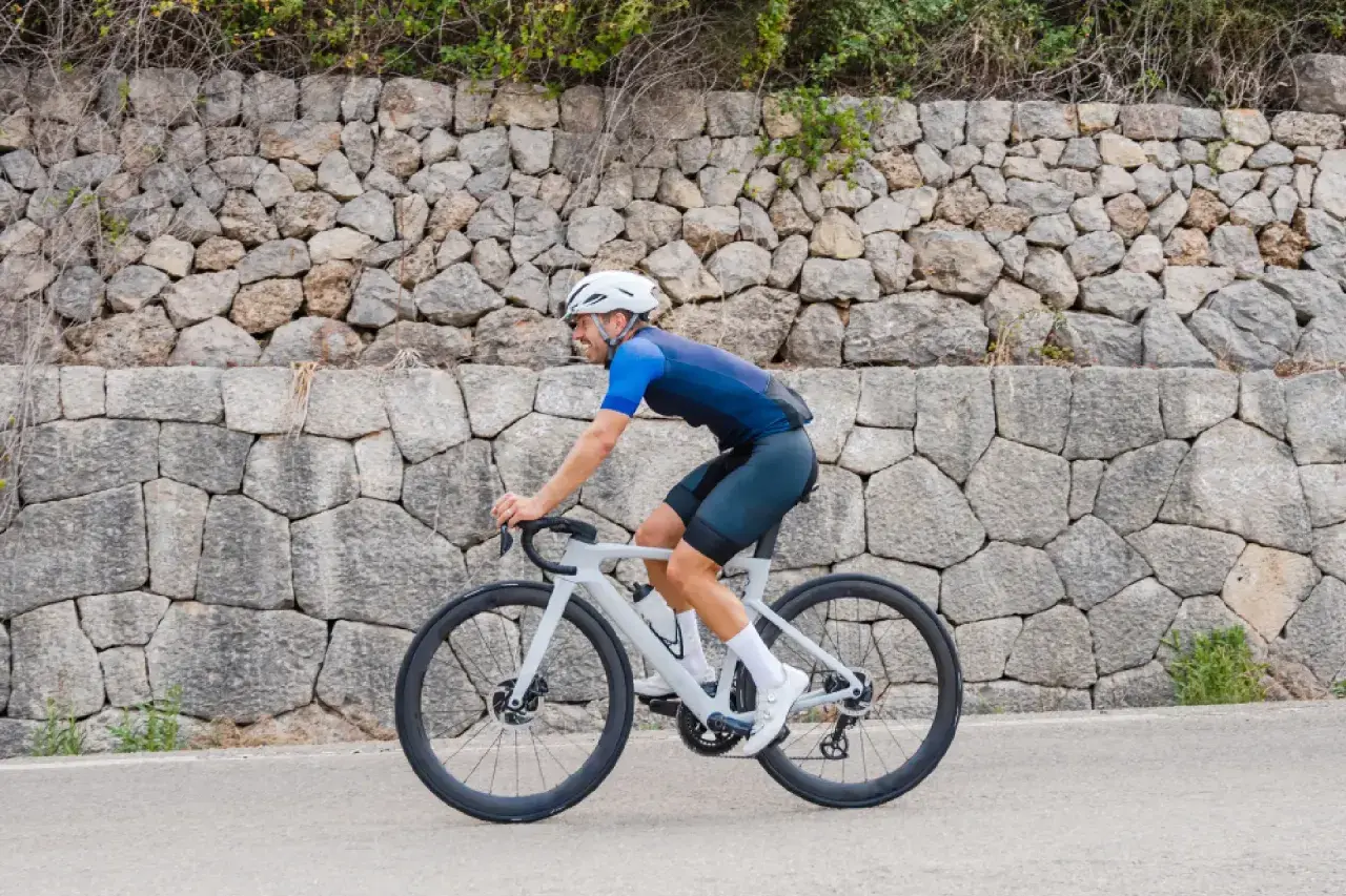 Ciclista pedaleando por una carretera en Mallorca en bici, con un muro de piedra detrás.