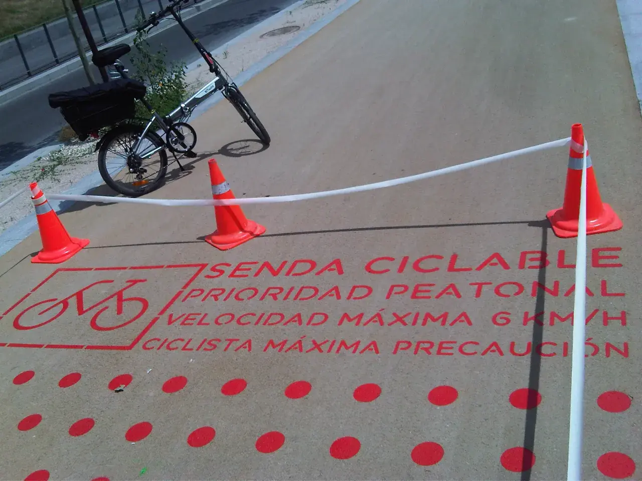 Bicicleta plegable en sendas ciclables con señalización de prioridad peatonal y límite de velocidad.