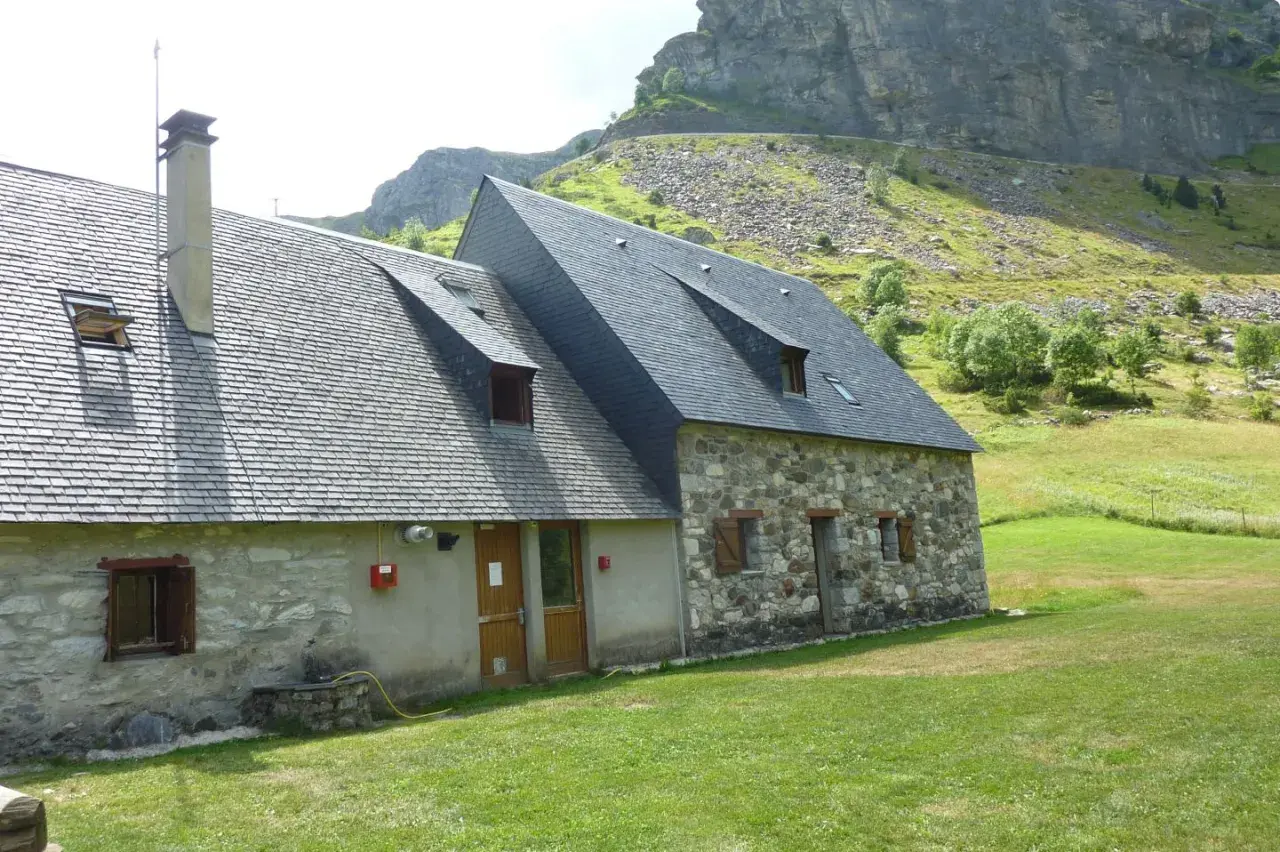 El refugio Vignemale, una construcción de piedra y pizarra, se alza en un prado verde bajo imponentes montañas rocosas.