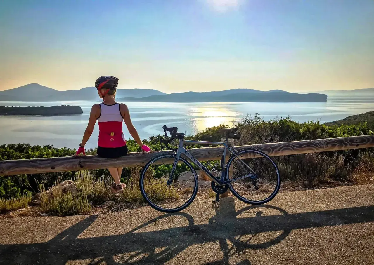Ciclista descansa tras un tour en bicicleta en Cerdeña, disfrutando de la vista al mar al atardecer.