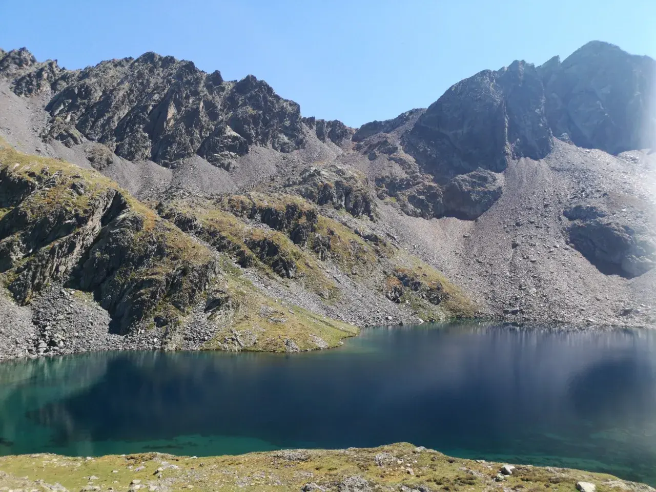 Lago sereno y montañas rocosas cerca del refugi de Baiau.