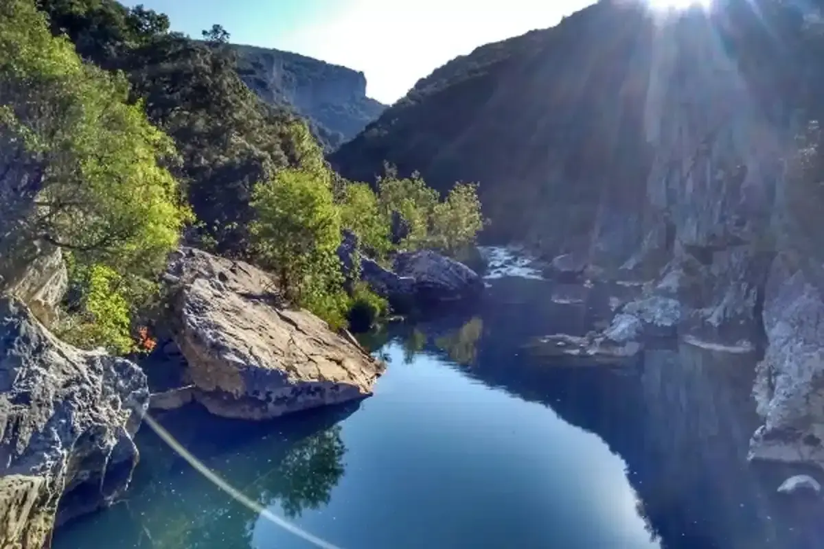 El río fluye sereno en la Foz de Lumbier, rodeado de imponentes rocas y vegetación exuberante bajo un sol radiante.