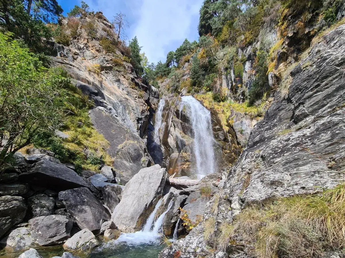 Cascada imponente en la ruta Rupit, rodeada de rocas y vegetación otoñal. El agua cae con fuerza sobre las piedras, creando un paisaje natural espectacular.