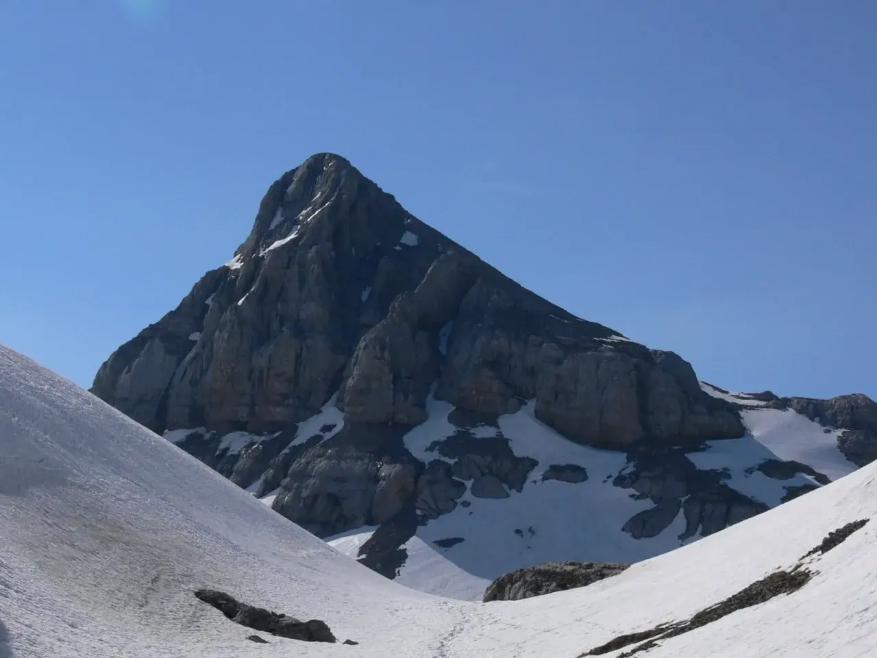 Majestuosa cumbre rocosa en el **valle de Belagua**, con nieve en sus laderas y un cielo azul intenso.