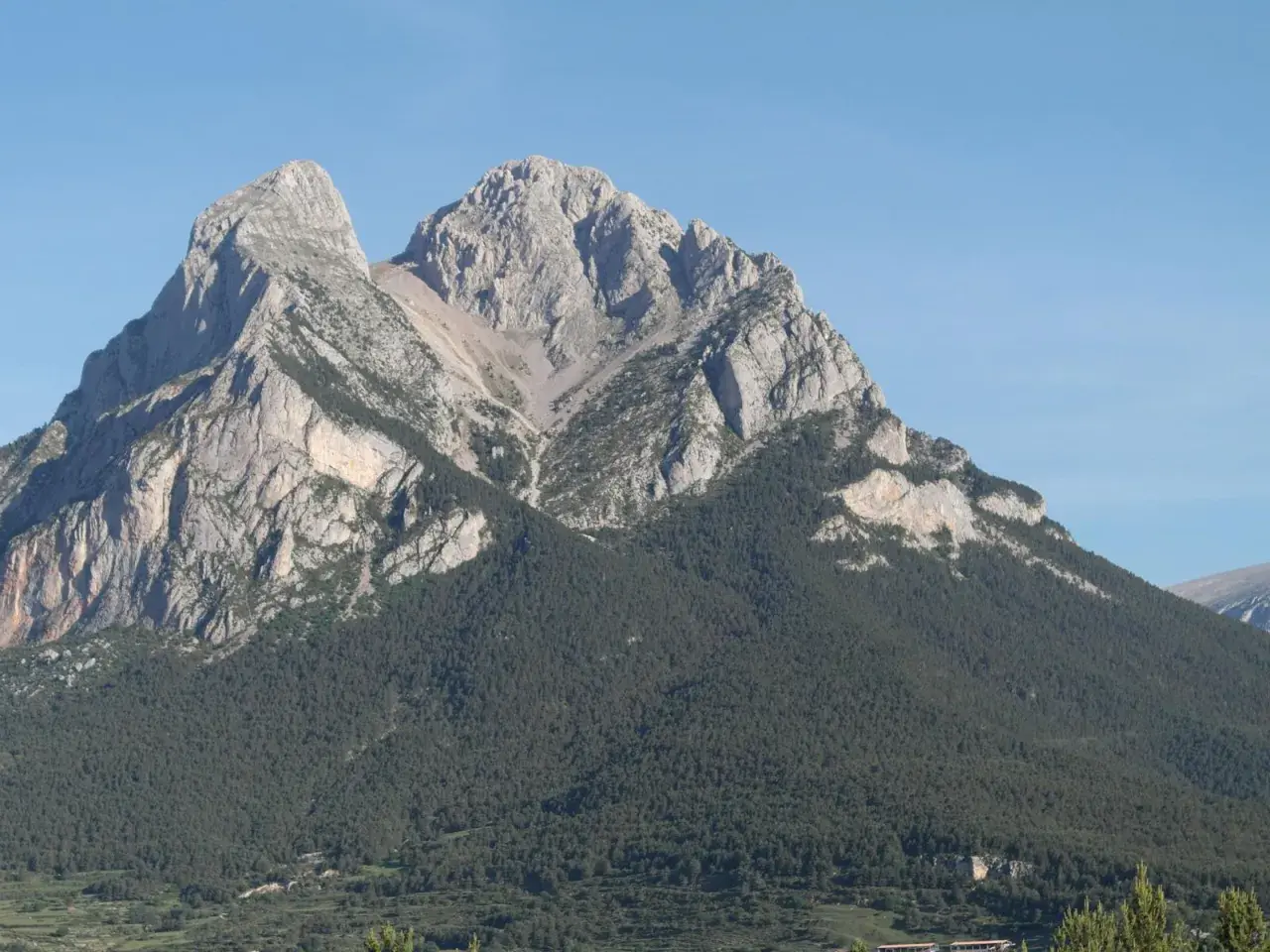 Majestuoso Pedraforca, cumbre rocosa coronada por pinos. Una ruta de senderismo desafiante espera.