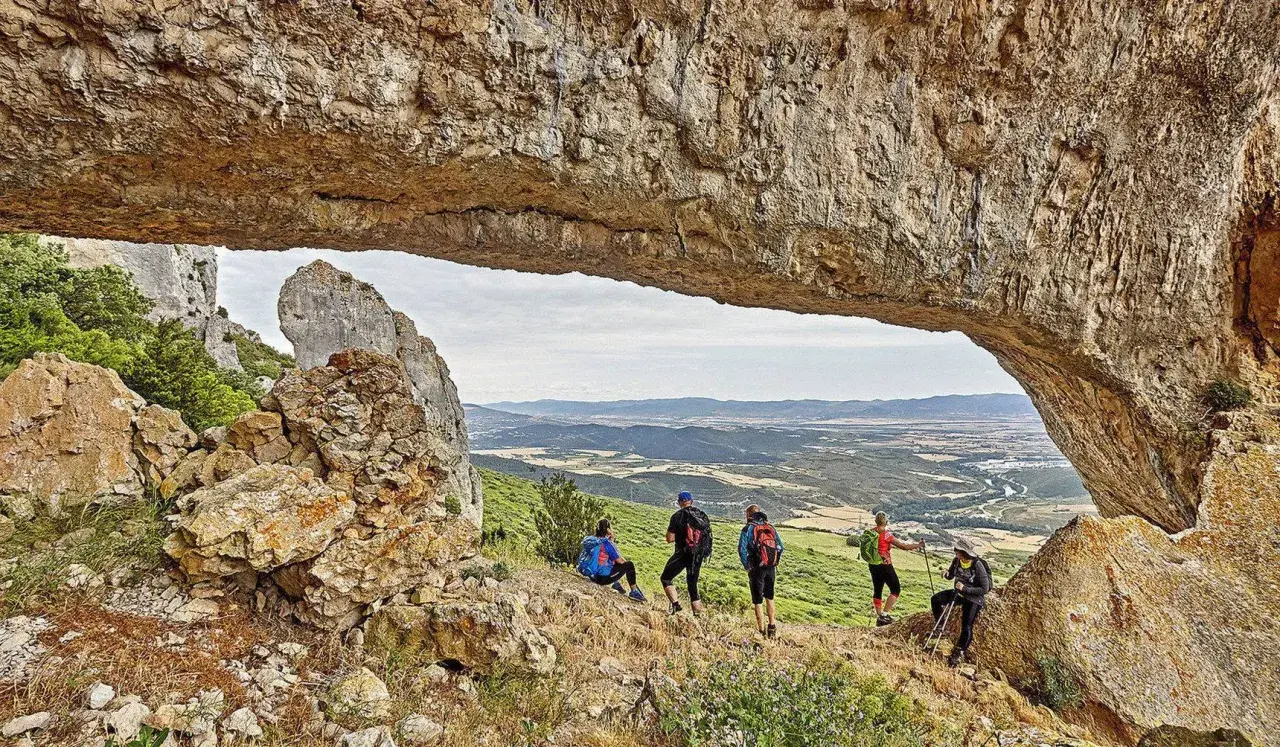 Senderistas disfrutan de vistas panorámicas en rutas por Navarra, bajo un arco natural de roca.