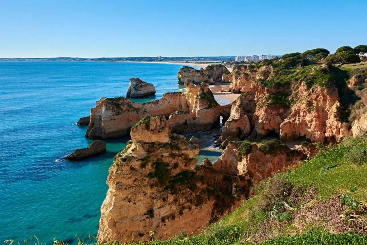 Acantilados dorados y mar turquesa en las **playas de Portugal**. Un paisaje idílico con formaciones rocosas y vegetación exuberante.