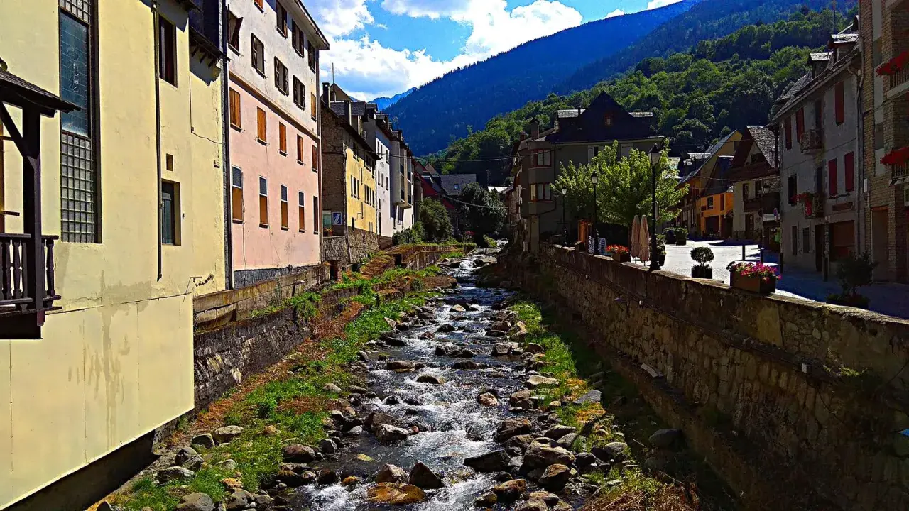 Un río serpentea entre casas de colores y montañas verdes. La **altitud vielha** se siente en el aire fresco y la vista panorámica.