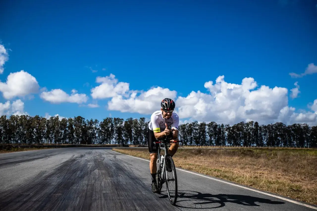Ciclista pedaleando en la Vía de la Plata en bici, con pulgares arriba bajo un cielo azul y nubes blancas.