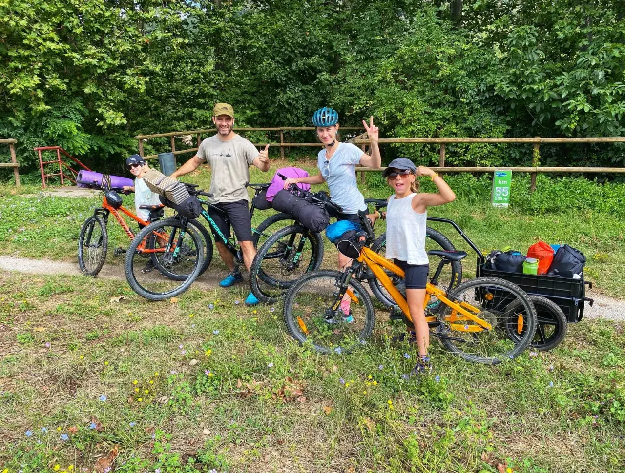 Familia lista para la ruta Pirinexus, con bicicletas y equipaje, disfrutando del paisaje verde.