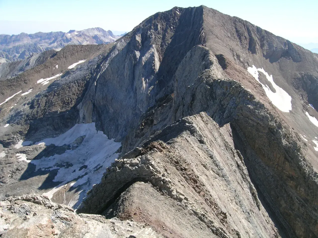 Cresta rocosa y escarpada, con restos de nieve, que se asemeja a un pico espadas en la inmensidad de las montañas.
