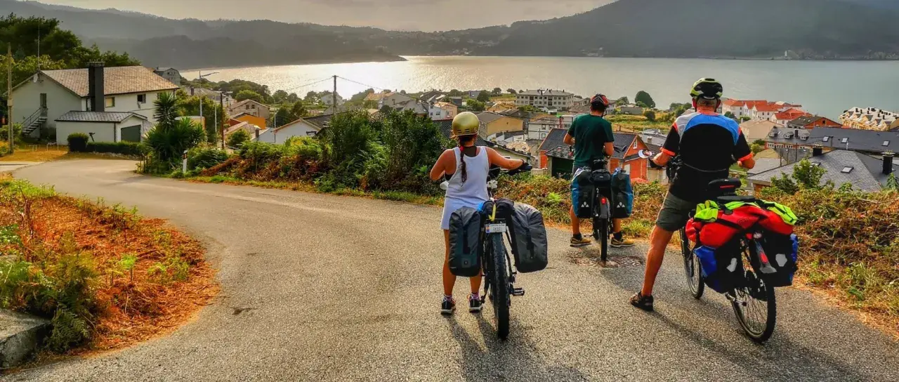 Ciclistas con alforjas exploran **rutas bicicleta** con vistas a un pueblo costero y el mar al atardecer.