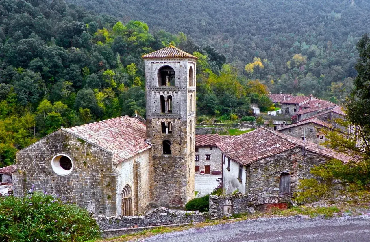 Iglesia románica y casas de piedra en un valle boscoso, ideal para explorar las rutas Camprodon.