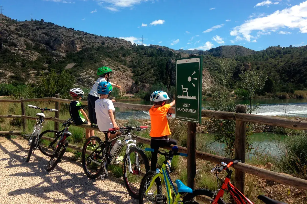 Niños en bicicleta disfrutan de la **vía verde Val de Zafán**, señalizada con un mirador panorámico.